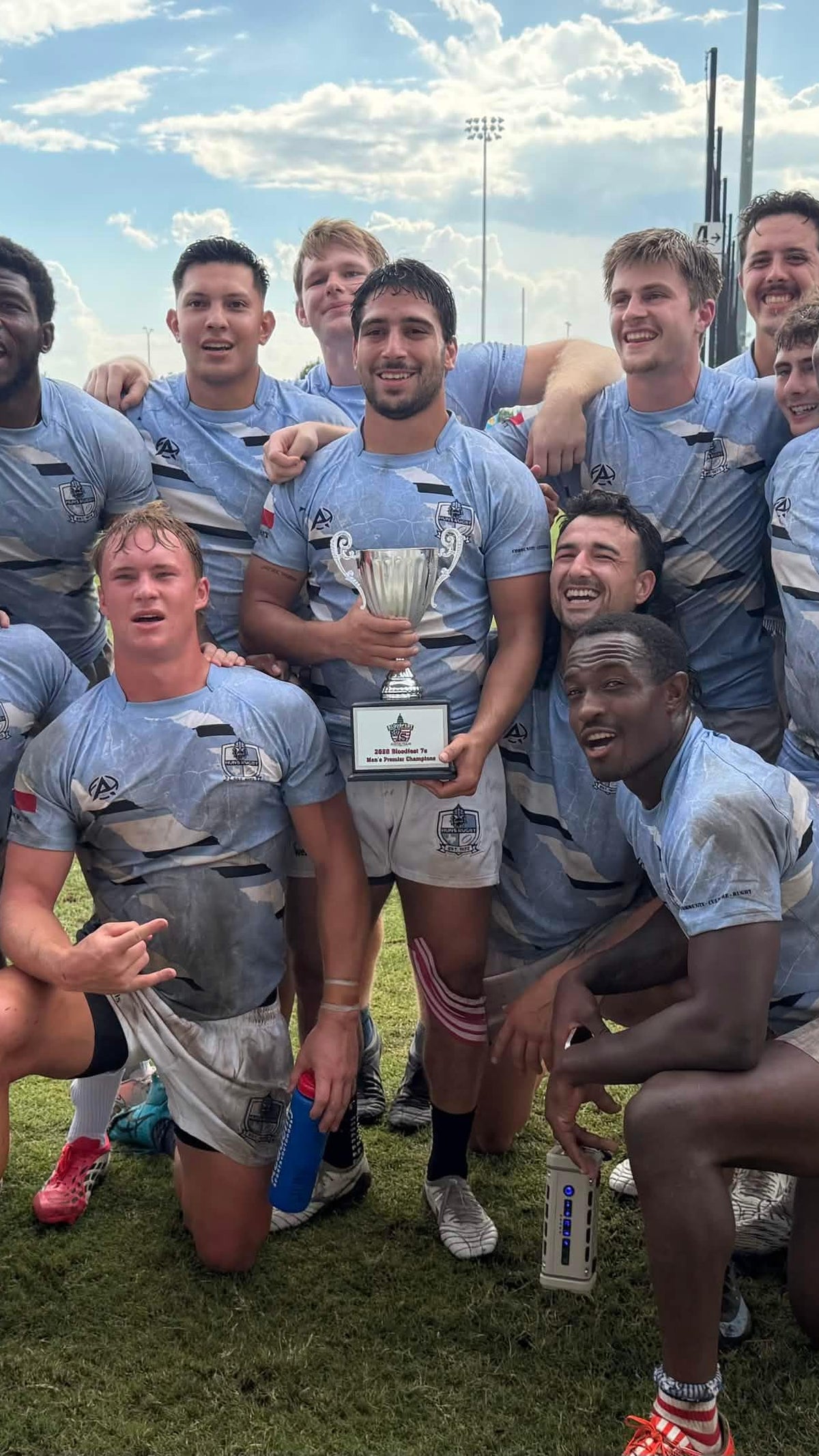 Rugby team in light blue jerseys celebrating with a trophy